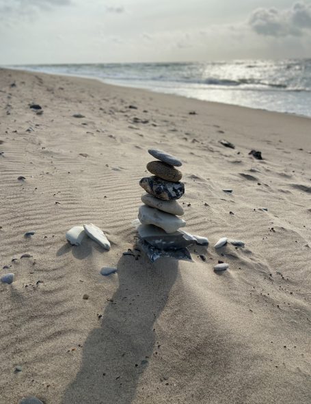 Entspannung - Ein Steinhaufen auf einem Sandstrand mit Wasser im Hintergrund.